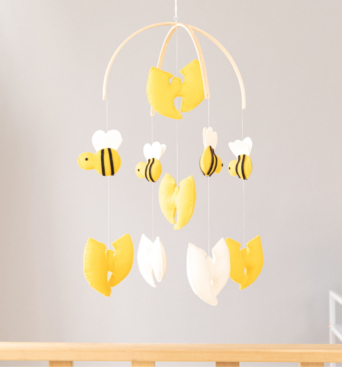 Crib mobile with puffy, yellow and white, felt Wu Tang-style W's and bumble bees hanging from a curved wood  frame
